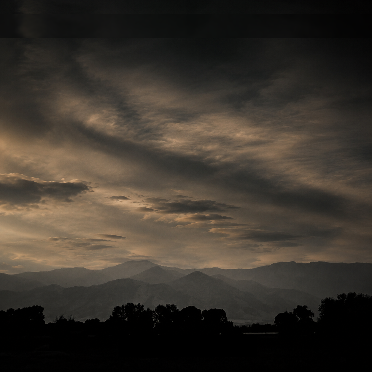 Layered Montana mountain ridgelines beneath a dramatic evening sky near Bozeman